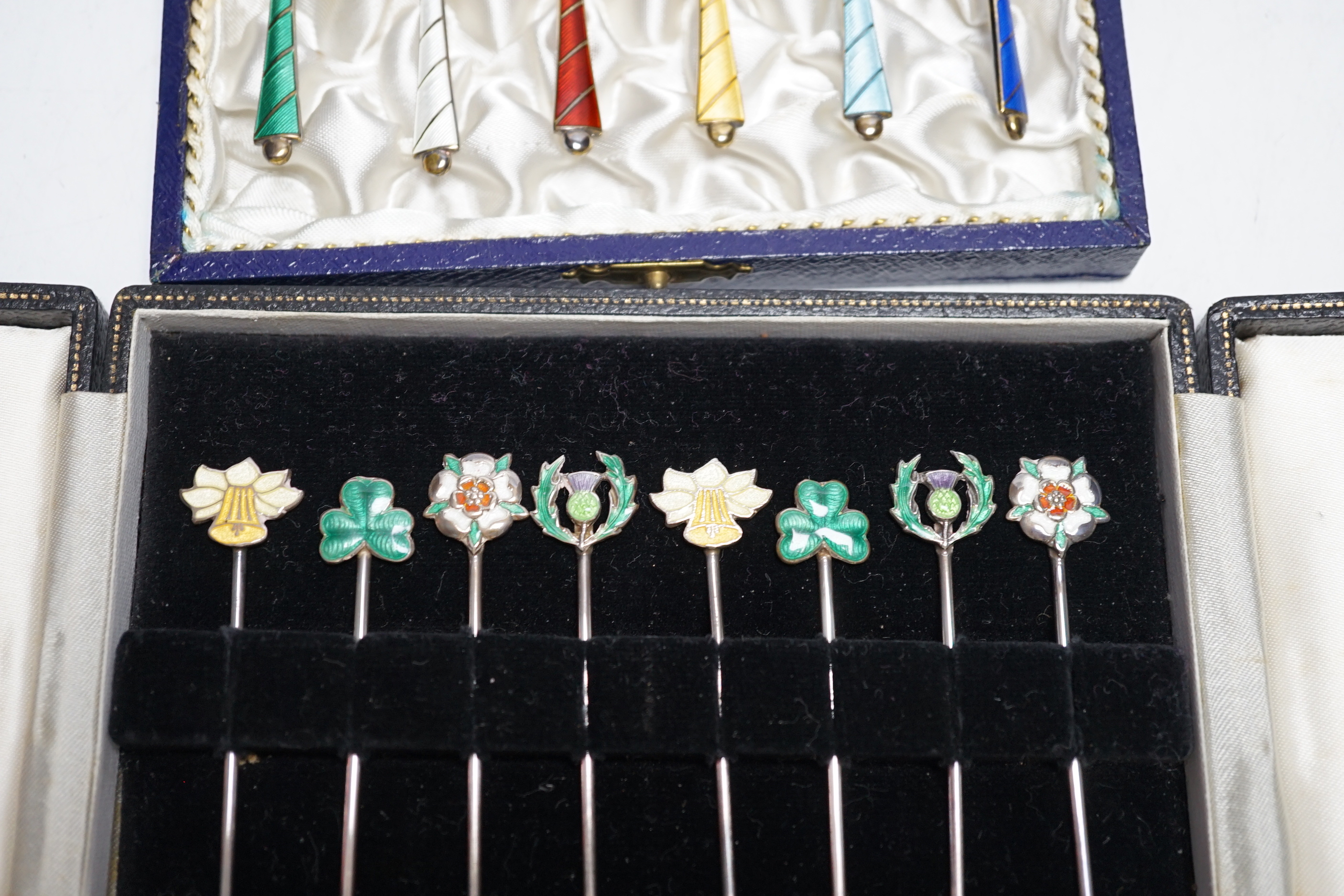 A cased set of six Danish gilt sterling and polychrome enamelled coffee spoons and a cased set of eight enamelled white metal cocktail sticks, stamped 'silver', the terminals decorated with the floral emblem of the count